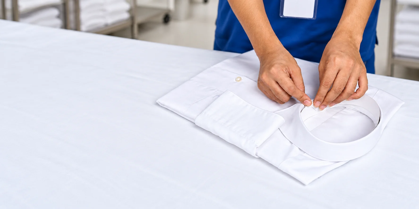 Ohana team member applying a finishing touch to the collar of a folded white shirt